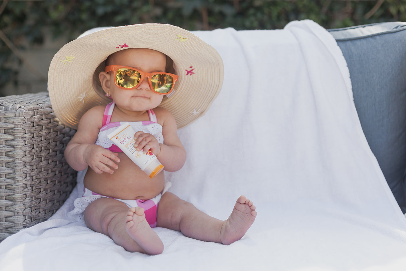 Baby girl in hat and sunglasses holding Earth Baby Broad Spectrum Sunscreen