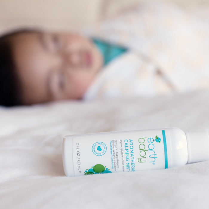 Non-Toxic, Hypoallergenic Aromatherapy Calming Mist on bed with sleeping baby in the background